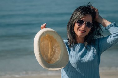 Sahilde dinlenen şapkalı gülümseyen genç bir kadının portresi.