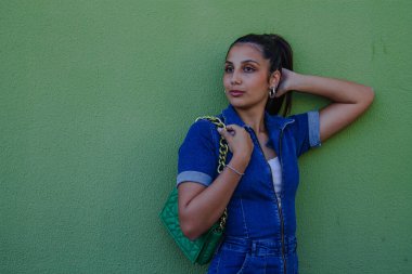 Duvarda duran yeşil çantalı çekici genç kadın.