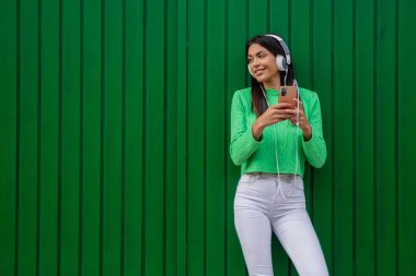 Duvarında kulaklıkları olan mutlu genç bir kadın.