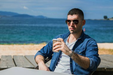 Genç adam plaj terasında kahve içiyor.