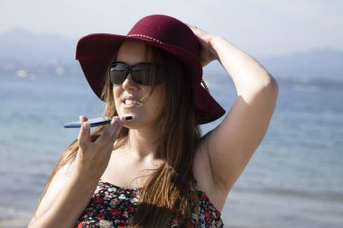 Kumsalda mutlu bir kadın cep telefonuyla sesli mesaj gönderiyor.