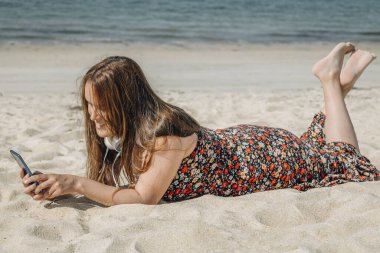 Güzel, iri yarı bir kadın plajda telefon ve kulaklıkla dinleniyor.