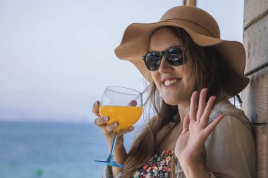 Güzel kıvrımlı kadın meyve suyu içiyor ve plaj barından el sallıyor.