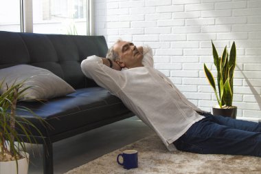 Olgun bir adam evde kahve içerken kanepede dinleniyor.