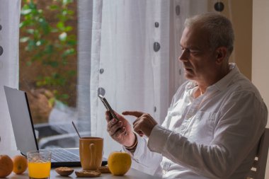 Olgun bir adam evde ya da iş yerinde kahvaltı yaparken çalışıyor.