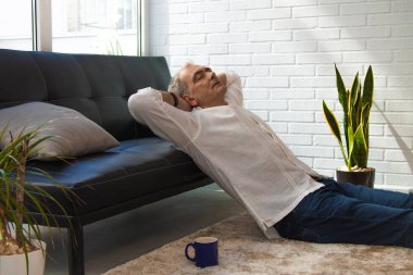 Olgun bir adam evde kahve içerken kanepede dinleniyor.