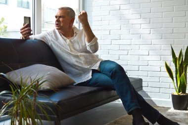 Cep telefonu ve zafer ya da başarı ifadesi olan olgun bir adam.