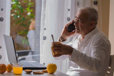 Olgun bir adam evde ya da iş yerinde kahvaltı yaparken çalışıyor.