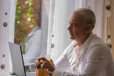 Yetişkin bir adam evde laptopla çalışırken kahvaltı yapıyor.