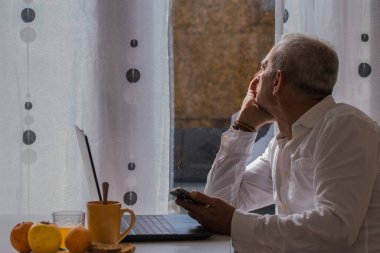 Depresyonda ve sıkılmış olgun bir adam kahvaltı yaparken ve evde çalışırken pencereden dışarı bakıyor.