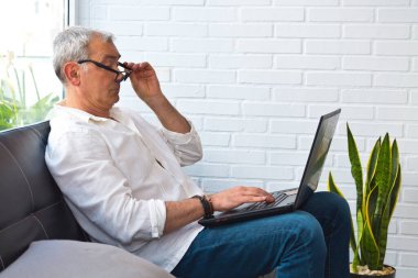 Bilgisayarla çalışan gözlüklü ve miyoplu orta yaşlı bir adam.