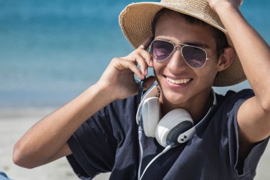 Kulaklıklı ve sahilde telefonla konuşan genç bir adam.