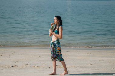 Genç kız sahilde meşrubat içiyor.