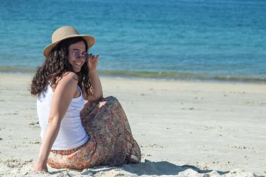 Genç bir kadın kumsalda rahatça oturuyor.