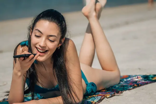 young woman on the beach and sending an audio message with the phone