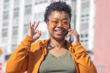 Afro-Amerikan kadın sokakta akıllı telefonuyla konuşuyor ve 