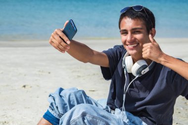 Genç adam selfie çekiyor ya da plajda telefonla canlı video çekiyor.