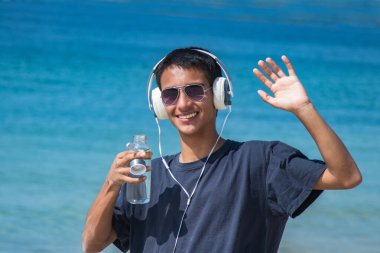 Kulaklıklı genç bir adam ve sahilde el sallayan bir şişe su.