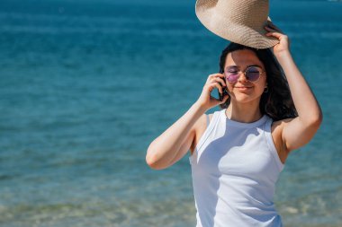 Kumsalda akıllı telefon kullanarak mutlu gülümseyen bir kız.