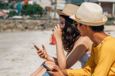 Kumsalda akıllı telefon kullanan genç bir çift.