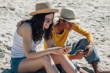 Kumsalda akıllı telefon kullanan genç bir çift.