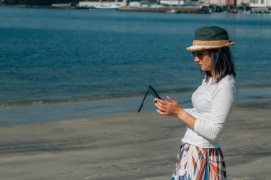 Sahilde cep telefonu kullanan genç bir kadın.