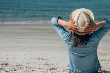 Kumsalda oturup denize bakan rahat genç bir kadın.