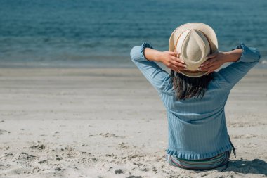 Kumsalda oturup denize bakan rahat genç bir kadın.