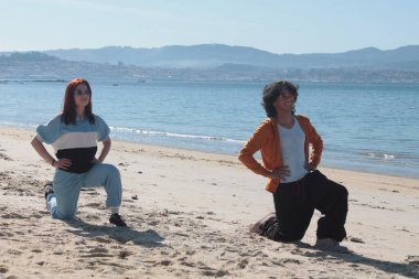 Çiftler plajda dinlenme egzersizleri yapıyor.