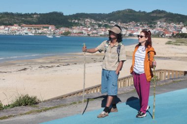 Sırt çantalı çift sahilde yürüyor ve eğleniyor.