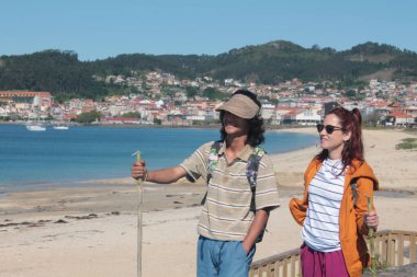 Sırt çantalı çift sahilde yürüyor ve eğleniyor.