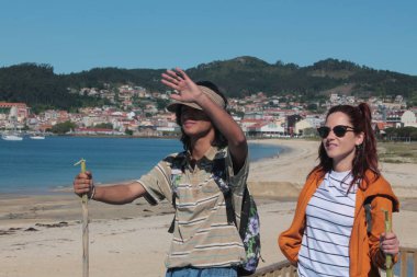 Sırt çantalı çift sahilde yürüyor ve eğleniyor.