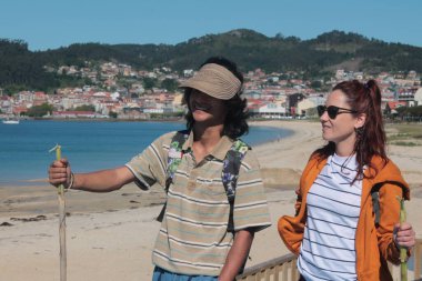 Sırt çantalı çift sahilde yürüyor ve eğleniyor.