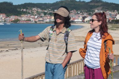 Sırt çantalı çift sahilde yürüyor ve eğleniyor.