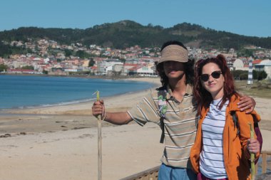 Sırt çantalı çift sahilde yürüyor ve eğleniyor.