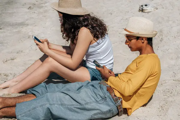 Kumsalda akıllı telefon kullanan genç bir çift.