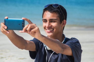 Genç adam selfie çekiyor ya da sahilde telefonla canlı video çekiyor.