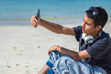 Genç adam selfie çekiyor ya da sahilde telefonla canlı video çekiyor.