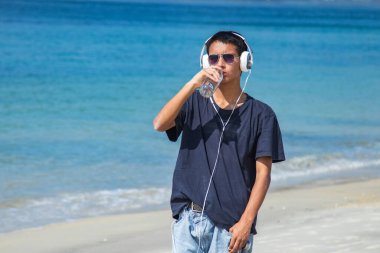 Sahilde kulaklıkları ve bir şişe suyu olan genç bir adam.