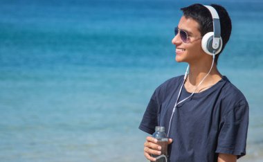 Sahilde kulaklıkları ve bir şişe suyu olan mutlu bir genç.