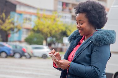 Kışın ceketli afro kadın sokakta cep telefonu kullanıyor.