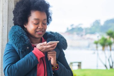 Sokakta cep telefonu kullanan afro bir kadın mesaj ya da ses gönderiyor
