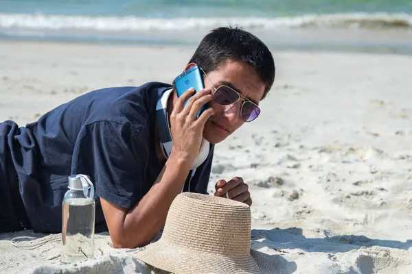 stock image young man with headphones talking on the phone on the beach