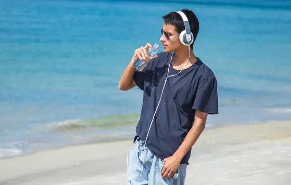 stock image young man with headphones and bottle of water on the beach