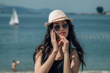 Kumsalda akıllı telefonuyla konuşan genç bir turist kadın.