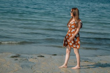 Sahilde yürüyen güneş gözlüklü genç bir kadın.