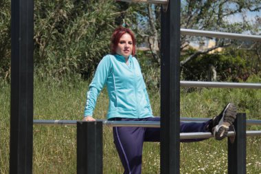 Kadın dışarıda parmaklıklarla spor yapıyor.