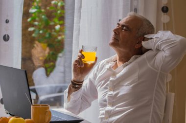 Rahatlamış olgun bir adam iş yerinde kahvaltı yapıyor.