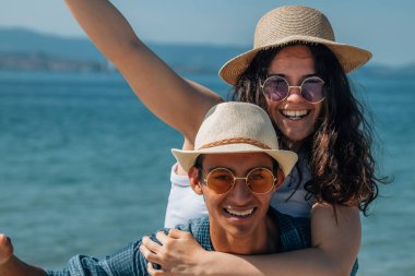 Mutlu bir adam, kadınını sırtında taşıyor ve tropik plajda gülüyor. Sırılsıklam aşık bir adam kız arkadaşına sarılıp eğleniyor. Neşeli çift denizde yazın tadını çıkarıyor. 