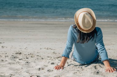 Kumsalda oturup denize bakan rahat genç bir kadın.